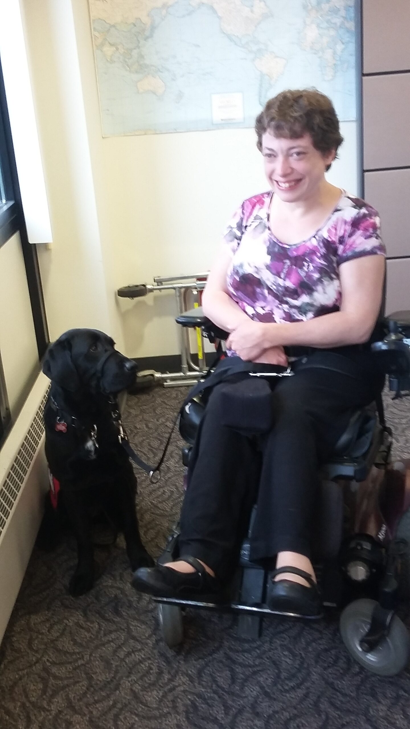 Tracy is smiling next to her mobility assist dog, Gidget.